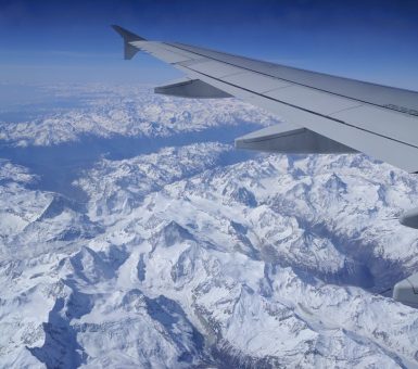 View of snow-covered mountains from an aircraft window with the wing in clear sight.